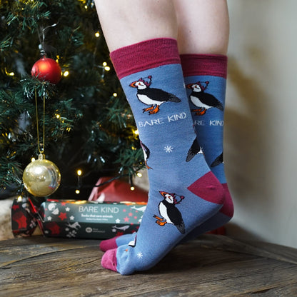 lifestyle image of model wearing blue christmas puffin bamboo socks in front of a christmas tree