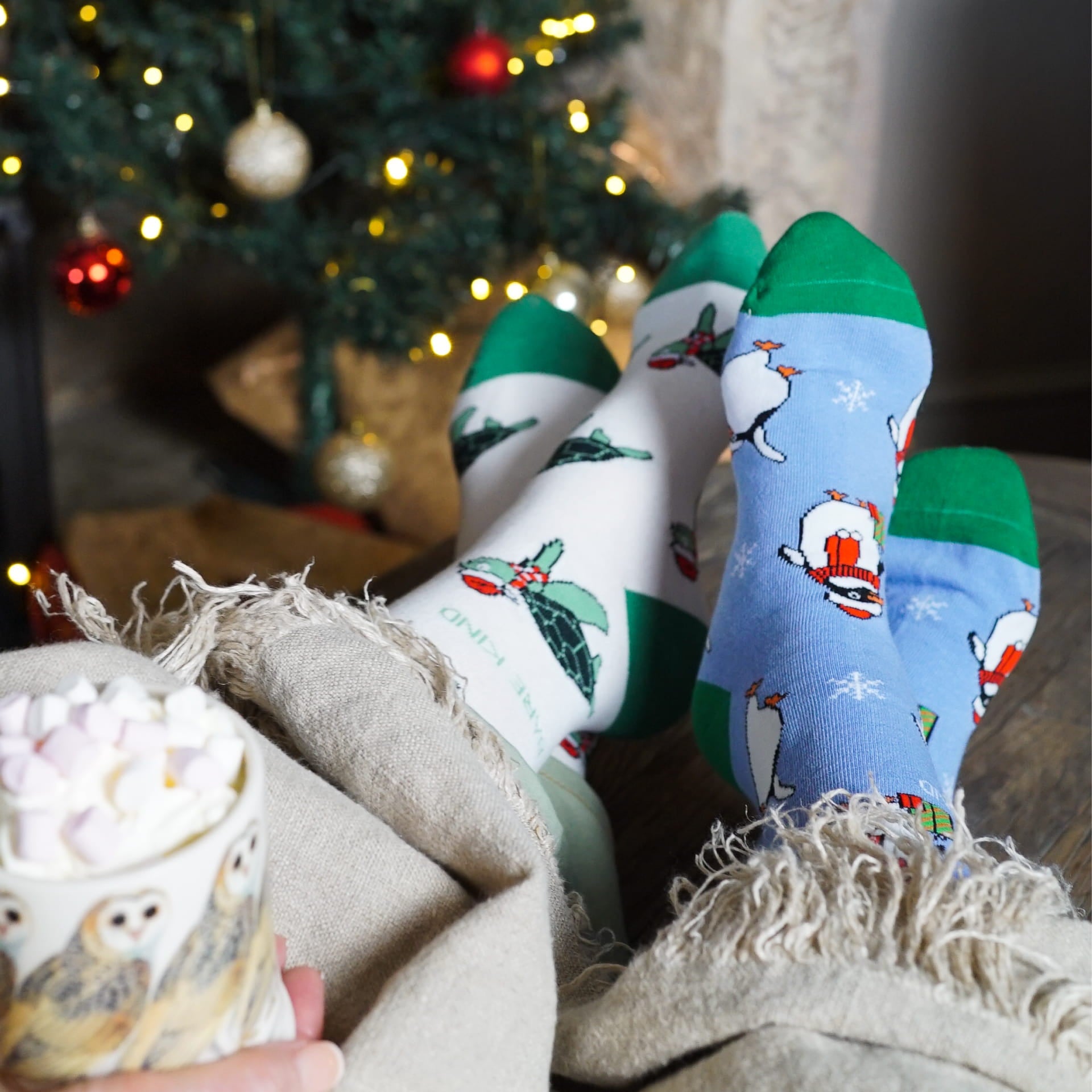 lifestyle image of models wearing christmas turtle and penguin bamboo socks with a blanket and christmas tree