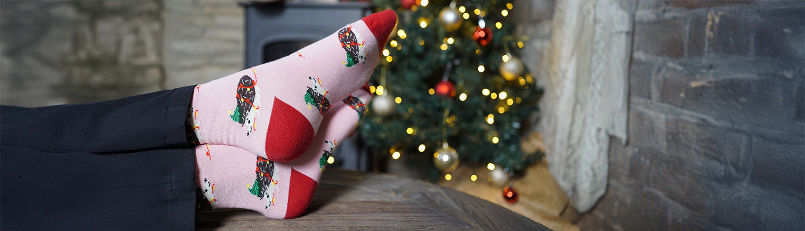 Person wearing festive socks with hedgehogs design in front of a decorated Christmas tree.