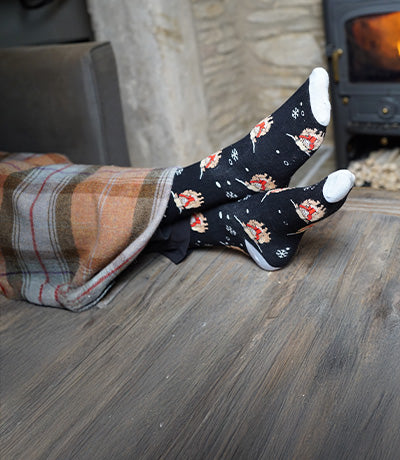 Person wearing socks with highland cows designs in front of a fireplace