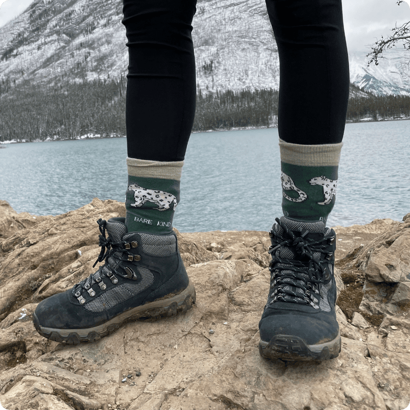 Person wearing hiking boots and snow leopard bamboo socks with a mountain and lake background