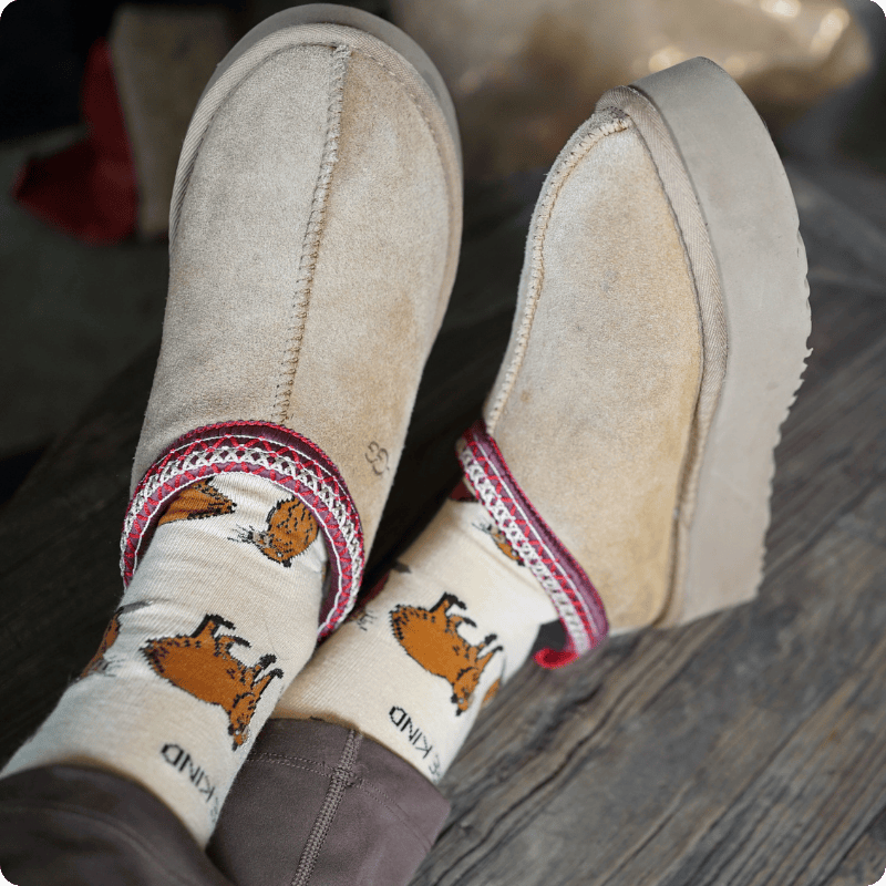 Beige slip-on shoes worn with capybara bamboo socks on a wooden floor.
