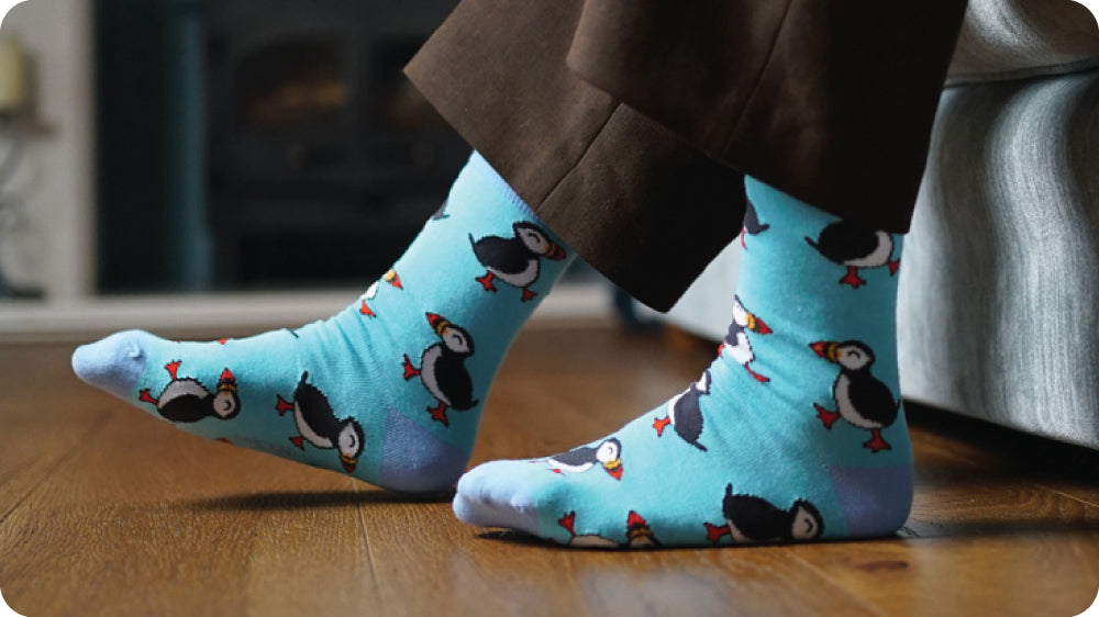 Blue socks with puffins pattern worn by a person on a wooden floor.