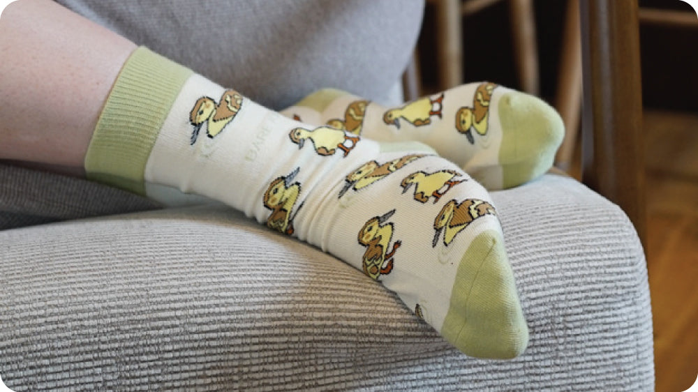 White socks with duck pattern worn by a person sitting on a chair.