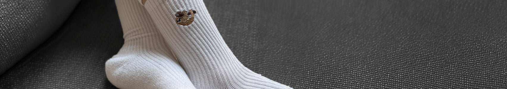 White socks with a small sloth on a dark fabric background