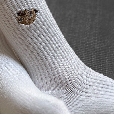 Close-up of a white sock with a small sloth design on a textured surface.