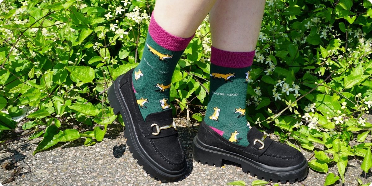 Person wearing black shoes and foxes bamboo socks with a green leafy background