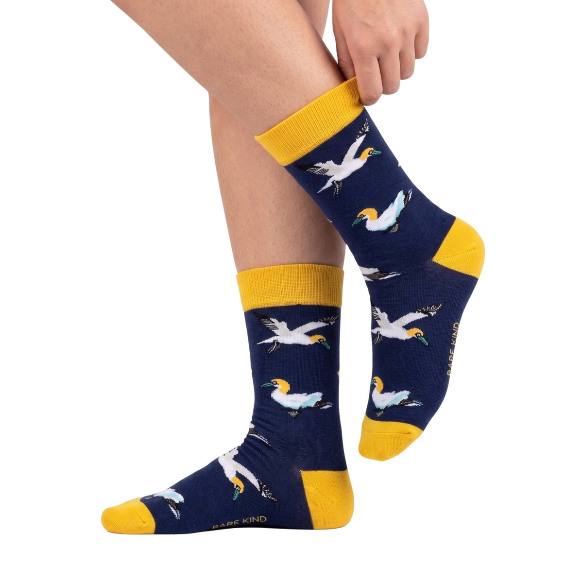 A person wearing navy crew socks with a repeating white bird print and bright yellow cuffs, heels, and toes, shown against a plain white background.