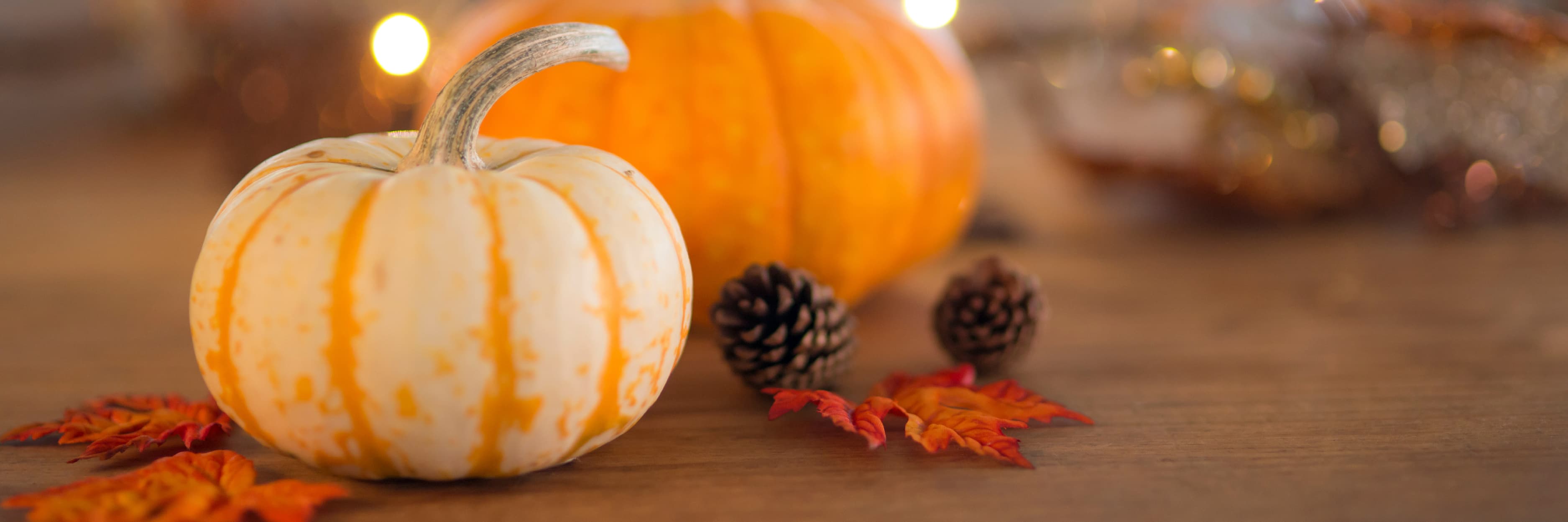 Small striped pumpkin with a larger orange pumpkin and pinecones on a wooden surface.