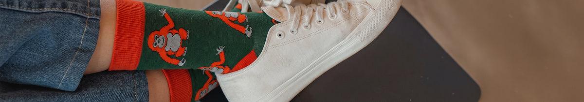 A pair of dark green crew socks with bright orange cuffs, heels, and toes, featuring a repeating pattern of orangutans in orange and gray.