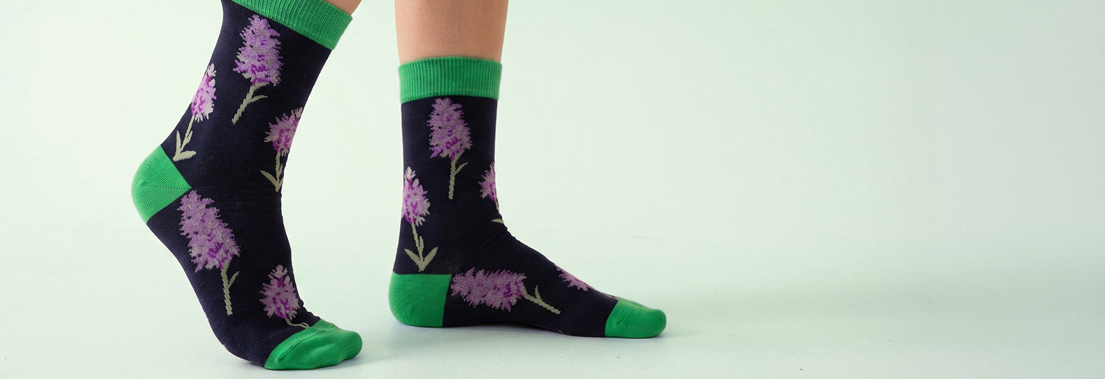 Navy socks with purple orchid patterns and green accents worn by a person on a light gray background