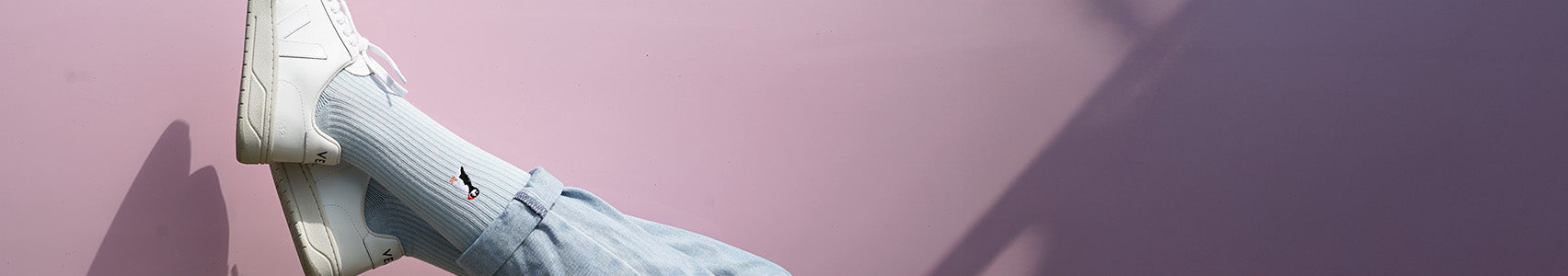 Person wearing light blue Puffins ribbed socks and white sneakers with a pink background