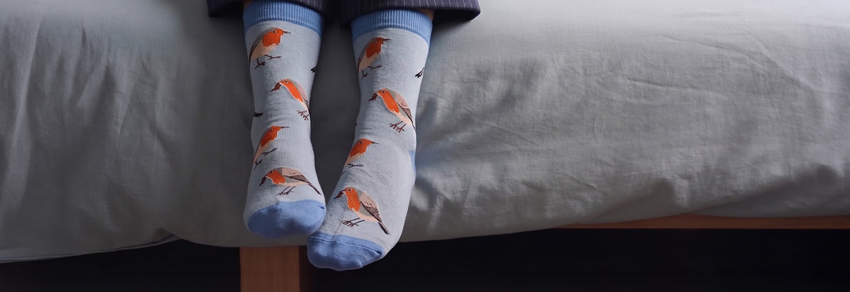 A person's legs dangling over a bed, wearing light blue socks with an orange and brown bird pattern.