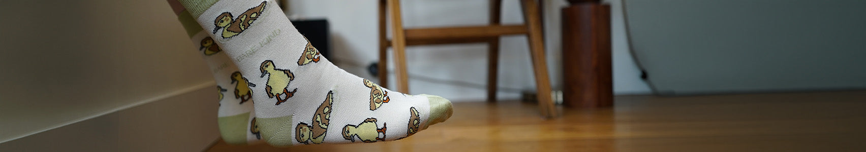Person wearing socks with ducklings design on a wooden floor