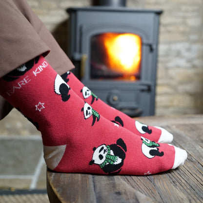 lifestyle image of model wearing red christmas panda bamboo socks in front of log fire