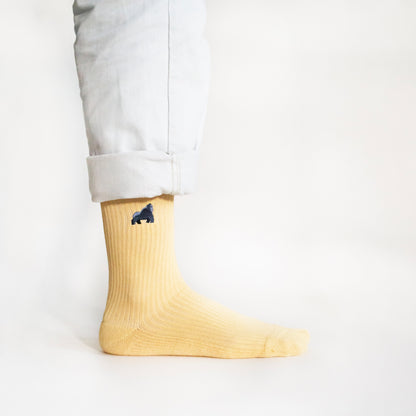 minimalist picture of model standing wearing pastel yellow ribbed bamboo socks with an embroidered elephant motif, side angle view