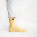 minimalist picture of model standing wearing pastel yellow ribbed bamboo socks with an embroidered elephant motif, side angle view