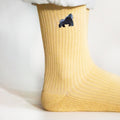 minimalist closeup picture of model standing wearing pastel yellow ribbed bamboo socks with an embroidered elephant motif, side angle view