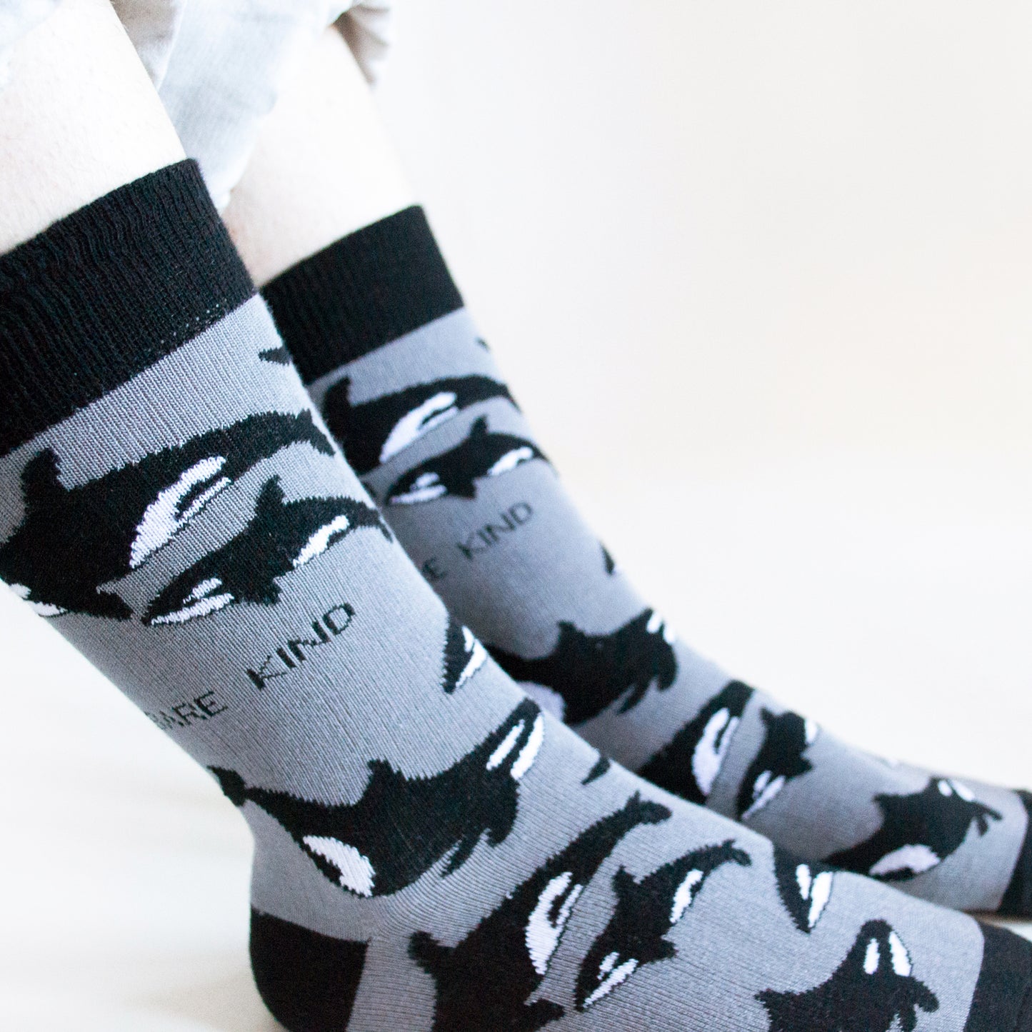 closeup of sitting model wearing black and grey orca bamboo socks, showing the woven orca design