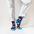 standing model wearing blue whale socks with left heel up, front view