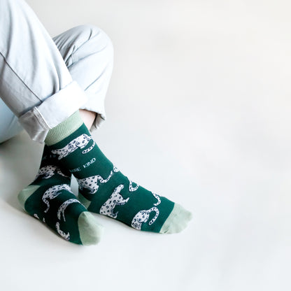 sitting model with ankles crossed wearing green snow leopard bamboo socks